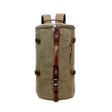 Bolso mochila de diseño cilíndrico confeccionado en tela canvas color verde oliva con detalles en cuero marrón. Cuenta con correas ajustables para usar como mochila, asas de mano, cierre superior y múltiples compartimentos con cierre.