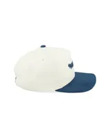 Gorra tipo trucker con corona estructurada en color crema y visera curva en color azul con textura aterciopelada. Presenta el logo de la marca bordado en el frente y detalle lateral.