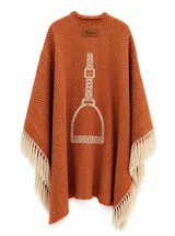 Ruana de tejido grueso con diseño de espiga en color naranja y detalles en beige. Presenta un bordado central de un estribo y flecos largos en los bordes.