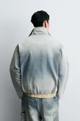 Cazadora relaxed fit de denim de algodón con efecto lavado degradado de azul a blanco. Tiene cuello subido, manga larga, bolsillos laterales en la costura de la cadera y acabados con elástico interior. El cierre frontal es con cremallera oculta por una solapa con botones a presión.
