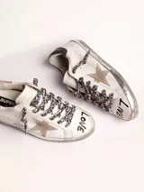 Zapatillas Golden Goose modelo Super-Star, de cuero blanco con efecto desgastado. Estrella de gamuza color beige en el lateral exterior y contrafuerte de cuero metalizado color dorado. Cordones con estampado animal print.