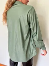 Camisa verde de cuero sintético con cuello clásico, cierre frontal con botones metálicos y dos bolsillos con solapa en el pecho.