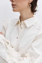 Camisa de color azul oscuro, con cuello clásico, cierre frontal de botones y detalle de volados en los hombros y a lo largo de las mangas largas.