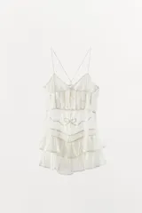 Vestido corto de viscosa y algodón, con escote en pico y tirantes finos cruzados en la espalda. Presenta un diseño con pliegues, aplicaciones de lazadas a contraste y falda con volantes en el bajo.