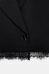 Blazer corto de corte recto con cuello solapa, manga larga y cierre frontal con un botón. Presenta detalles de encaje a tono en el ruedo y en los puños, con forro interior.