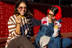 Remera de manga larga con diseño de rayas horizontales en color marrón y blanco, cuello redondo en contraste amarillo y estampa frontal con letras coloridas.