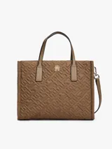 Cartera tipo tote de Tommy Hilfiger, confeccionada en nailon reciclado color marrón con diseño acolchado de monograma TH. Cuenta con dos asas superiores, cierre de cremallera y logo metálico distintivo en la parte frontal.