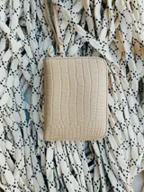 Billetera pequeña de cuero con textura efecto cocodrilo, cierre metálico perimetral y correa de muñeca extraíble. Incluye detalle de moneda metálica decorativa.
