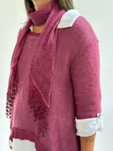 Sweater de punto color magenta con diseño asimétrico, cuello redondo y detalle de encaje bordado en el frente. Incluye una bufanda del mismo tejido y color, y se presenta superpuesto sobre una camisa blanca de algodón.