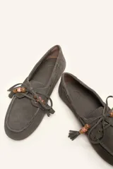 Mocasín estilo náutico de gamuza marrón, con cordones de cuero, borla decorativa y cuentas de colores en el empeine.