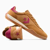 Championes Converse Run Star Trainer Ox color mostaza, con detalles en fucsia y blanco. Presentan el logo de la estrella y el chevrón en fucsia en el lateral, y suela de goma con diseño ondulado.