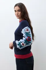 Sweater de punto color azul marino con diseño jacquard floral en las mangas y detalle de cuello redondo en color rojo. Presenta un corte holgado y mangas tres cuartos.