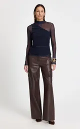 Blusa de manga larga confeccionada en microtul azul marino, con cuello alto y diseño ajustado. Presenta un corte asimétrico en el escote y detalles drapeados en el lateral, con transparencias en mangas y hombros.