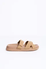 Sandalias planas color beige con dos tiras cruzadas en el empeine decoradas con tachas metálicas, suela ancha y diseño cómodo.
