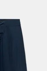 Pantalón de tiro medio con diseño tipo pareo, confeccionado en tejido satinado con acabado arrugado. Presenta pernera recta, cierre frontal con botón a presión y cremallera lateral oculta.