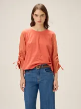 Remera color salmón con cuello redondo y mangas tres cuartos fruncidas con cordones ajustables en los puños.