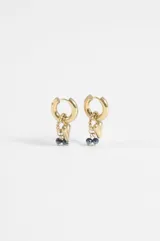 Aros de acero quirúrgico dorado con diseño de argolla y dijes colgantes que incluyen un corazón, una cadena trenzada y pequeñas cuentas oscuras facetadas.