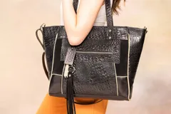 Bolso tote bag negro con diseño estructurado, que combina cuero liso, cuero grabado tipo cocodrilo y gamuza. Incluye doble asa de hombro, correa larga regulable y desmontable, llavero con flecos, bolsillo frontal con cierre y bolsillo trasero con cierre. El interior cuenta con forro de tela beige, bolsillo con cierre, divisor central con cierre y porta celular.