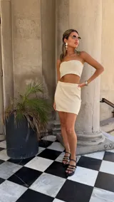 Vestido largo de tejido de red blanco, con apliques de flores negras en relieve. Lleva tirantes finos y tiene un corte recto con abertura lateral. Se usa sobre una prenda interior blanca.