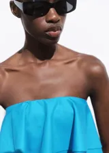 Top corto tipo palabra de honor, con diseño de volantes en capas y cierre de cremallera en la parte posterior.