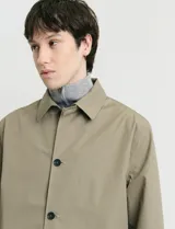 Gabardina clásica de corte recto, color beige, con cuello camisero, cierre frontal de botones y bolsillos laterales. Confeccionada en tejido técnico repelente al agua y al viento.