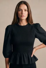 Blusa negra de algodón peinado, con cuerpo fruncido tipo smock, cuello redondo con volados y mangas largas abullonadas.