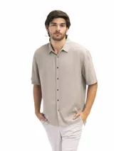 Camisa de manga corta color verde oliva, confeccionada en lino y viscosa, con cuello clásico y cierre frontal con botones. Corte suelto y estilo casual.