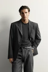 Blazer de corte regular fit color gris oscuro, confeccionado en tejido con lana. Cuenta con cuello con solapas de muesca, cierre frontal con tres botones, bolsillos con solapa en la cadera y un bolsillo de vivo en el pecho.