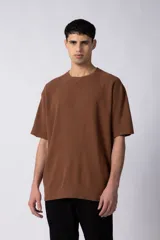 Remera de corte oversized en color marrón, confeccionada en tejido de algodón con textura de micropanal. Presenta cuello redondo con detalle de costura en forma de X y mangas cortas de estilo caído.