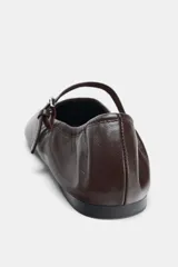 Zapato tipo bailarina de piel color marrón con efecto soft, tira delantera con hebilla metálica, suela plana y acabado en punta redonda.