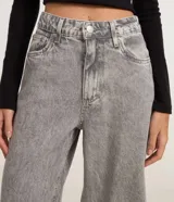 Pantalón wide leg de tiro alto en denim gris, con cierre de botón y cremallera, trabillas para cinturón y bolsillos delanteros y traseros.
