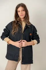 Campera de jean oversize color negro, con corte largo, cuello camisero, cierre frontal con botones metálicos y bolsillos frontales. Presenta un parche de cuero con logo en el pecho.