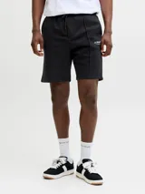 Bermuda deportiva negra de calce relajado, con cintura elástica ajustable mediante cordón, bolsillos laterales y costuras frontales en relieve. Presenta un pequeño estampado de texto en la pierna izquierda.
