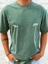 Remera de algodón color verde oscuro con efecto gastado (acid wash). Presenta un estampado minimalista en el pecho con el texto "ON THE MOVE" y un patrón de cuadros blancos a la derecha.