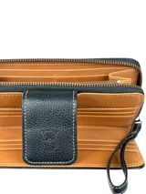Billetera grande de cuero negro con textura de reptil y detalles de costuras en contraste. Cuenta con solapa frontal con cierre magnético y correa de muñeca extraíble.