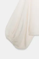 Cuerpo de punto negro con cuello barco, sisa ancha y mangas largas amplias con puños ajustados.