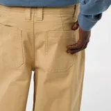 Pantalón de sarga color beige, de corte ancho y tiro alto, con cierre frontal y bolsillos laterales.