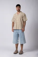 Camisa de manga corta tejida al crochet con diseño de rayas verticales negras sobre una base color crudo. Presenta cuello solapa y cierre frontal con botones.