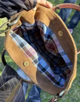 Cartera amplia de cuero gamuza en color marrón tostado, con asas de cuero marrón y aplique de caballo en pelo natural. Cuenta con correa ajustable y herrajes metálicos dorados.