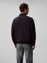 Buzo Calvin Klein azul marino de tejido terry, con cuello alto, cierre frontal parcial con cremallera, mangas largas, puños y ruedo acanalados. Cuenta con el logo de la marca bordado en el pecho.