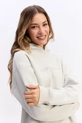 Canguro de algodón color beige con capucha amplia y corte relajado. Presenta un estampado rectangular en la espalda con motivos florales en tonos azules y el texto 'Harmony of Bloom'.