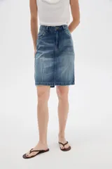 Falda de jean estilo clásico con bolsillos frontales y traseros, tiro alto y lavado azul medio con efecto desgastado.
