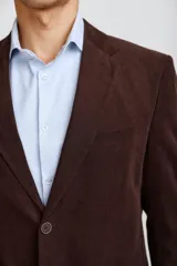 Blazer de pana color marrón oscuro, con cierre frontal de dos botones, solapas clásicas y bolsillos laterales con solapa. Presenta un diseño estructurado y elegante.