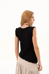 Blusa negra sin mangas con textura arrugada, cuello redondo y detalle de volados en los hombros. Presenta un corte asimétrico en el ruedo.