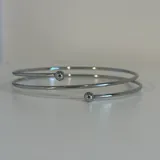 Brazalete rígido plateado con terminaciones en forma de esfera.