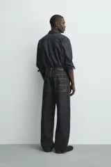 Pantalón chino de denim de algodón rígido, color índigo oscuro sin lavar. Corte baggy fit, tiro medio, con bolsillos frontales y traseros de plastrón. Presenta bordados a contraste en la cintura y en el bolsillo trasero.