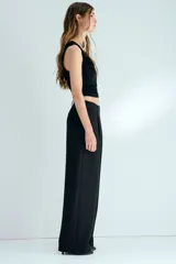 Pantalón sastrero negro de corte holgado, con diseño cruzado asimétrico en el frente, pinzas y piernas amplias.