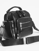 Mochila bandolera de cuero sintético color marrón, con múltiples compartimentos frontales y laterales con cierre metálico. Cuenta con asa superior y correas ajustables para usar como mochila o bandolera.