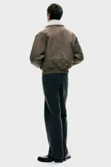 Campera bomber de nylon color marrón, ligeramente acolchada, con cuello de peluche blanco y cierre frontal. Incluye un bolsillo con cierre en una manga, bolsillos laterales con solapa y botón a presión oculto, y un bolsillo interior con botón a presión. Tiene remate acanalado ancho en puños y bajo, y un corte holgado.