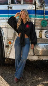 Camisa negra de lino con mangas largas abullonadas, diseño de nudo frontal y bordado de sol en color rojo en el pecho.